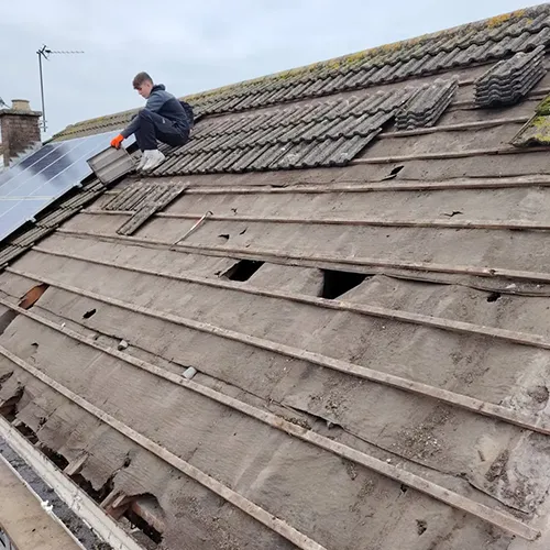 A man on a roof fixing a solar panel.