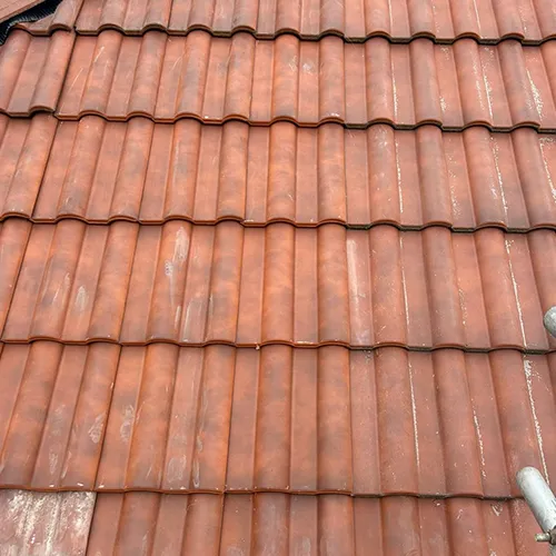 A cat sitting on top of a red tiled roof.